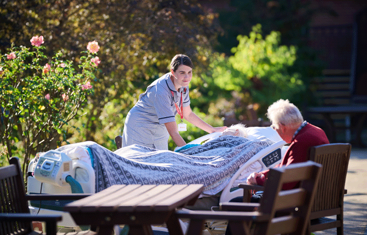 nurse smiling standing next to a patient in bed in the garden