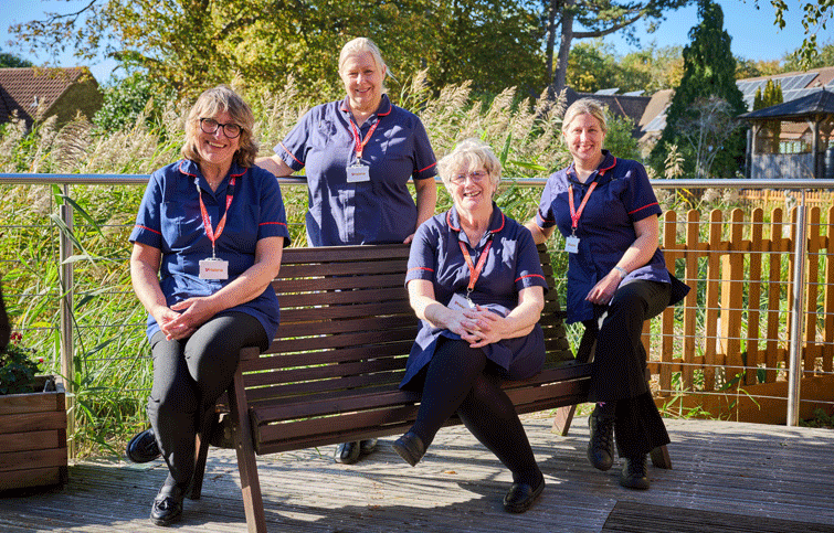 Four clinical nurse specialists sitting on the decking in the St Helena Hospice garden