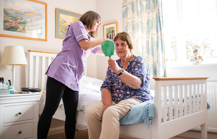 A healthcare professional from Radfield Home Care in support of St Helena wearing a lilac uniform assists a female client with styling their hair.