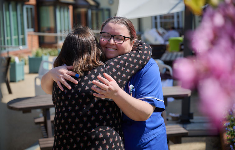 Image: Nurse smiling and hugging family member in the garden at St Helena Hospice