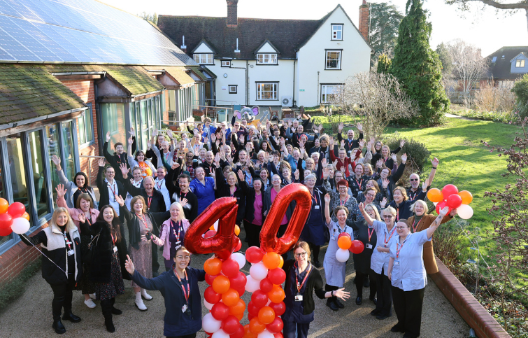 Around 100 St Helena staff and volunteer in the Hospice garden with their hands in the air and two nurses at the front holding red and orange balloons and a 4 and 0 balloon