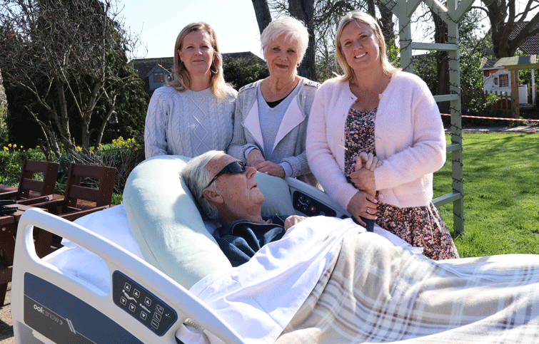 Image: Ted is in a hospice bed out in St Helena Hospice garden with his wife and two daughters next to him