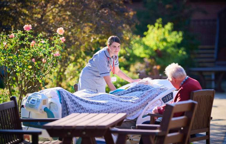 Hospice patient in a bed that has been wheeled into the garden so the patient can enjoy the outside whilst being in comfort and surrounded by their loved ones