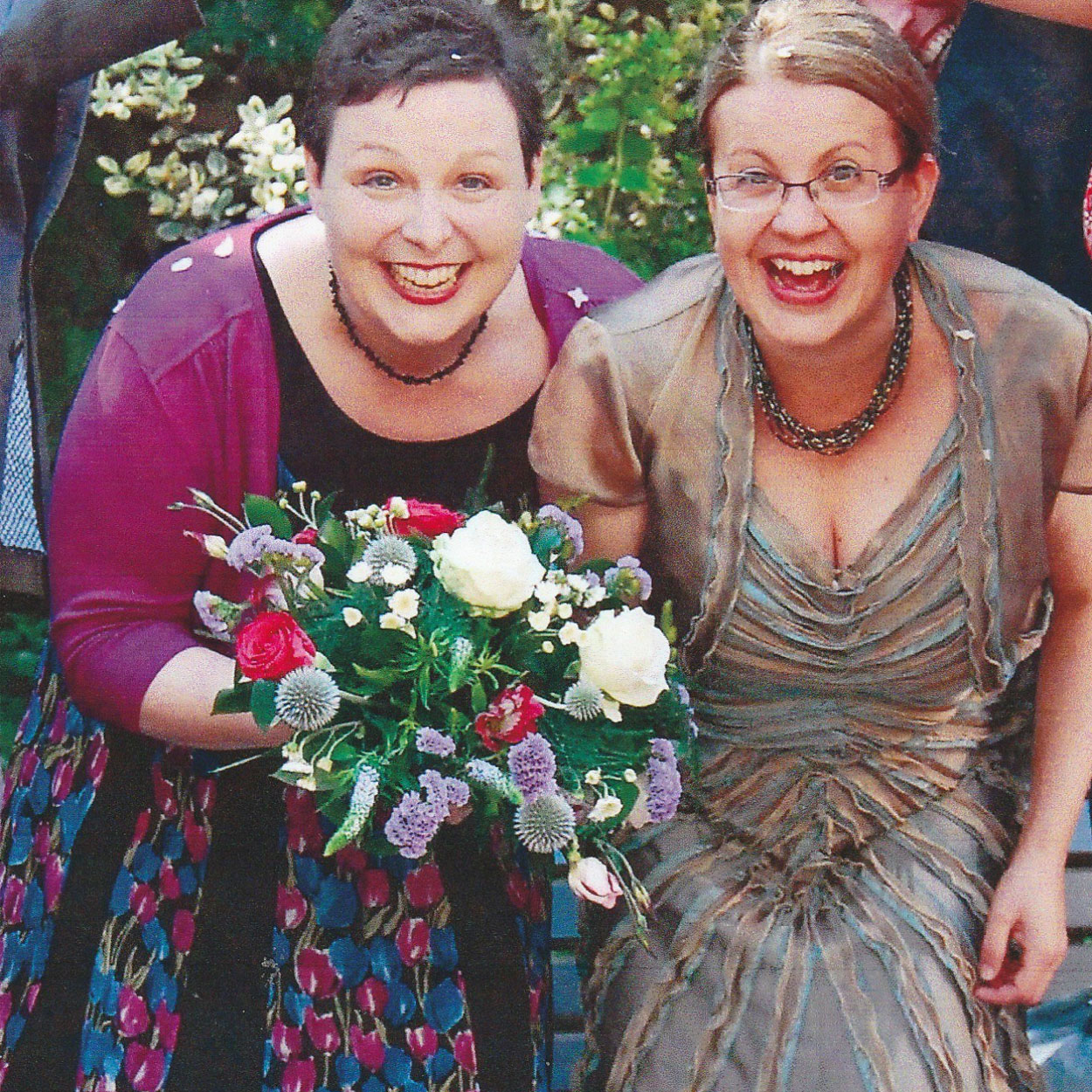 Viv and Rachel on their wedding blessing day, Viv is holding a bouquet of flowers, they are both smiling