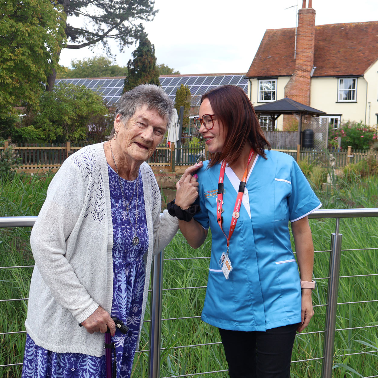 Good Days Community Club client with St Helena Care & Support assistant in front of St Helena Hospice