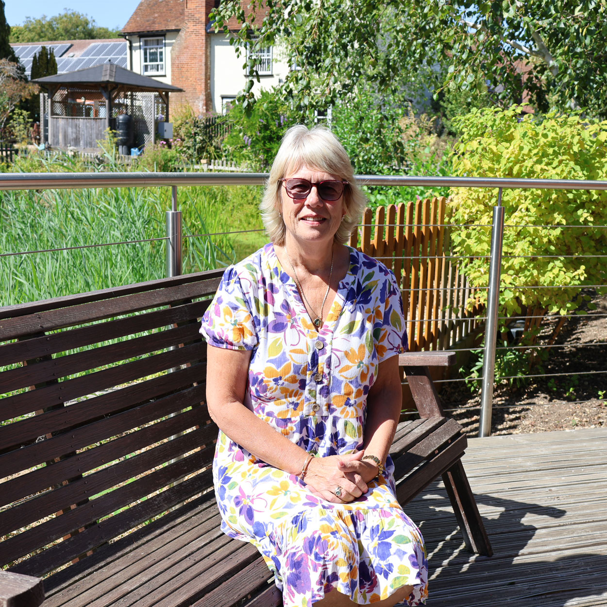 Sharon sitting on a garden bench with St Helena Hospice