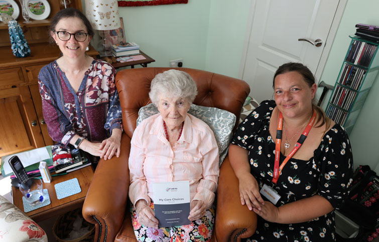 Kay sits in a chair with her daughter and Lindsey from St Helena Hospice either side of her