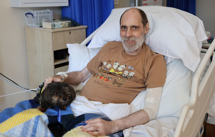 Bradley sits up in his St Helena Hospice bed with his little dog beside him