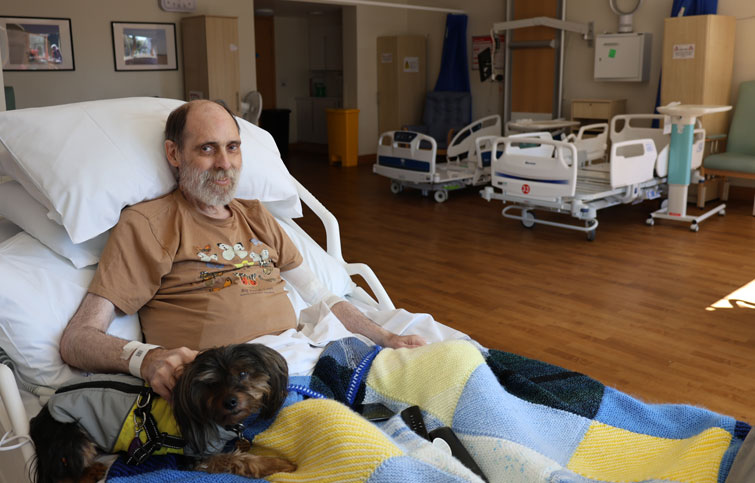 Bradley sits up in his St Helena Hospice bed with his little dog beside him